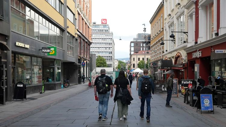 To menn og en kvinne fotografert bakfra mens de spaserer i en gate med mange bygninger rundt.