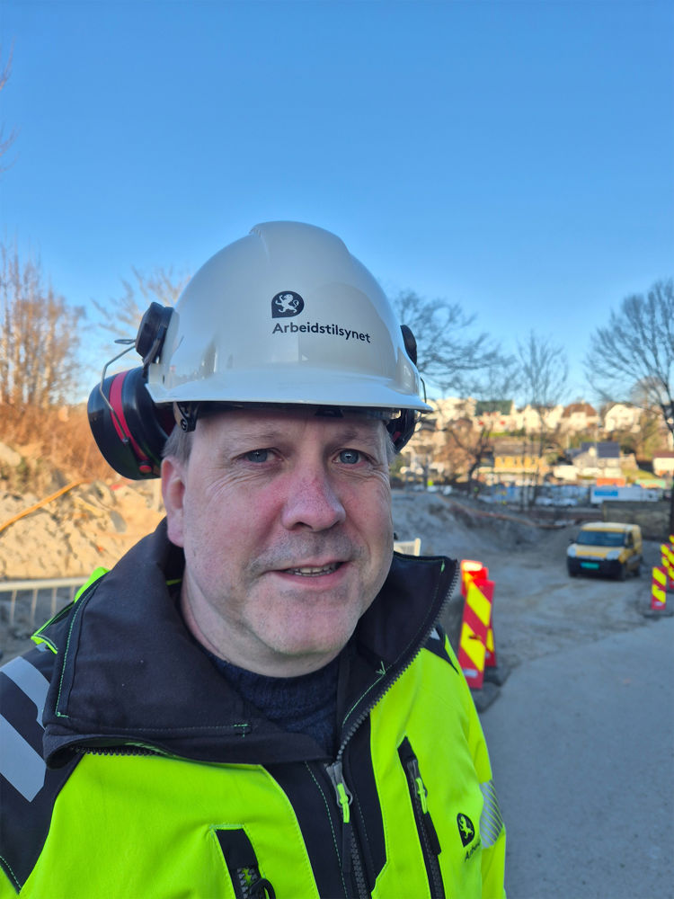 Mann i arbeidsklær og hjelm ser i  kamera 
